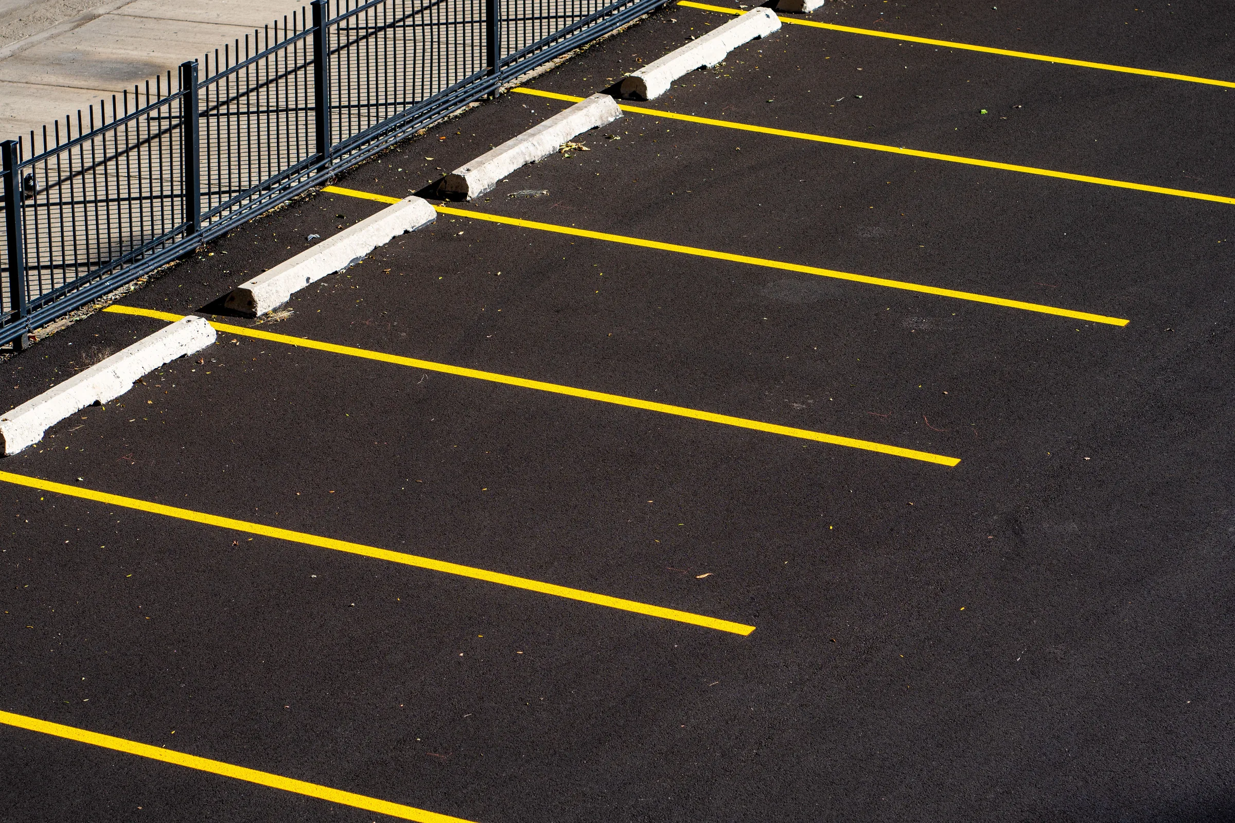 Newly striped parking lot with yellow lines and white curbs next to black metal fence.