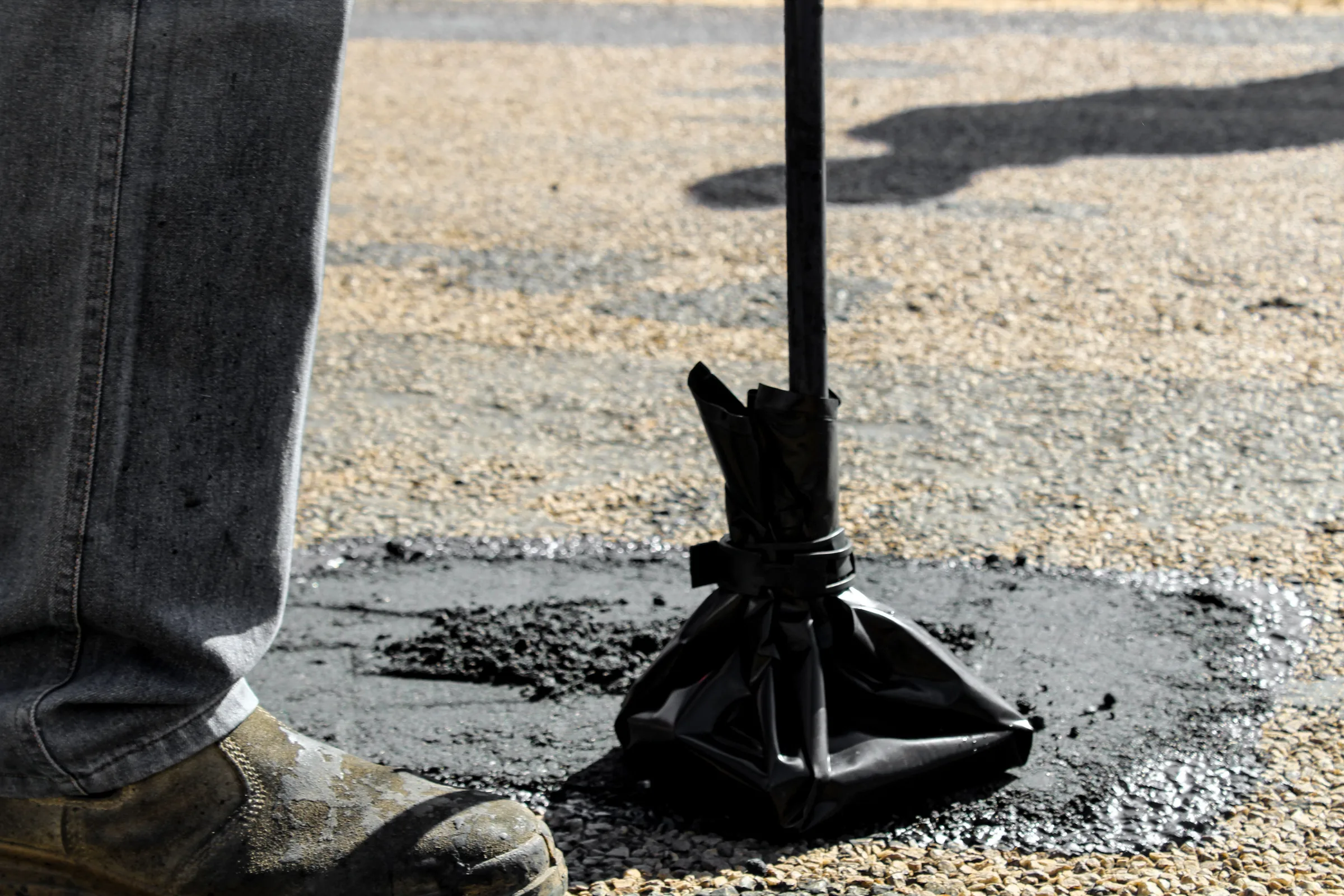 Person in work boots using a shovel to clear gravel and debris from pavement.