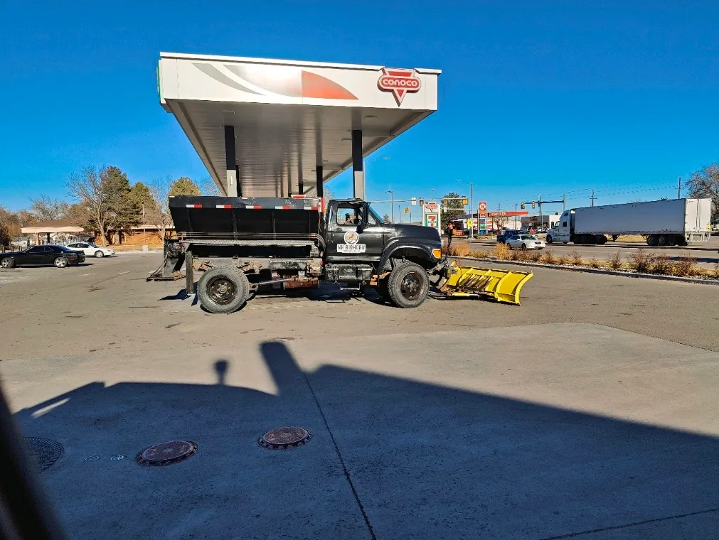 Snow removal truck with plow attachment parked at Conoco gas station in clear daylight.