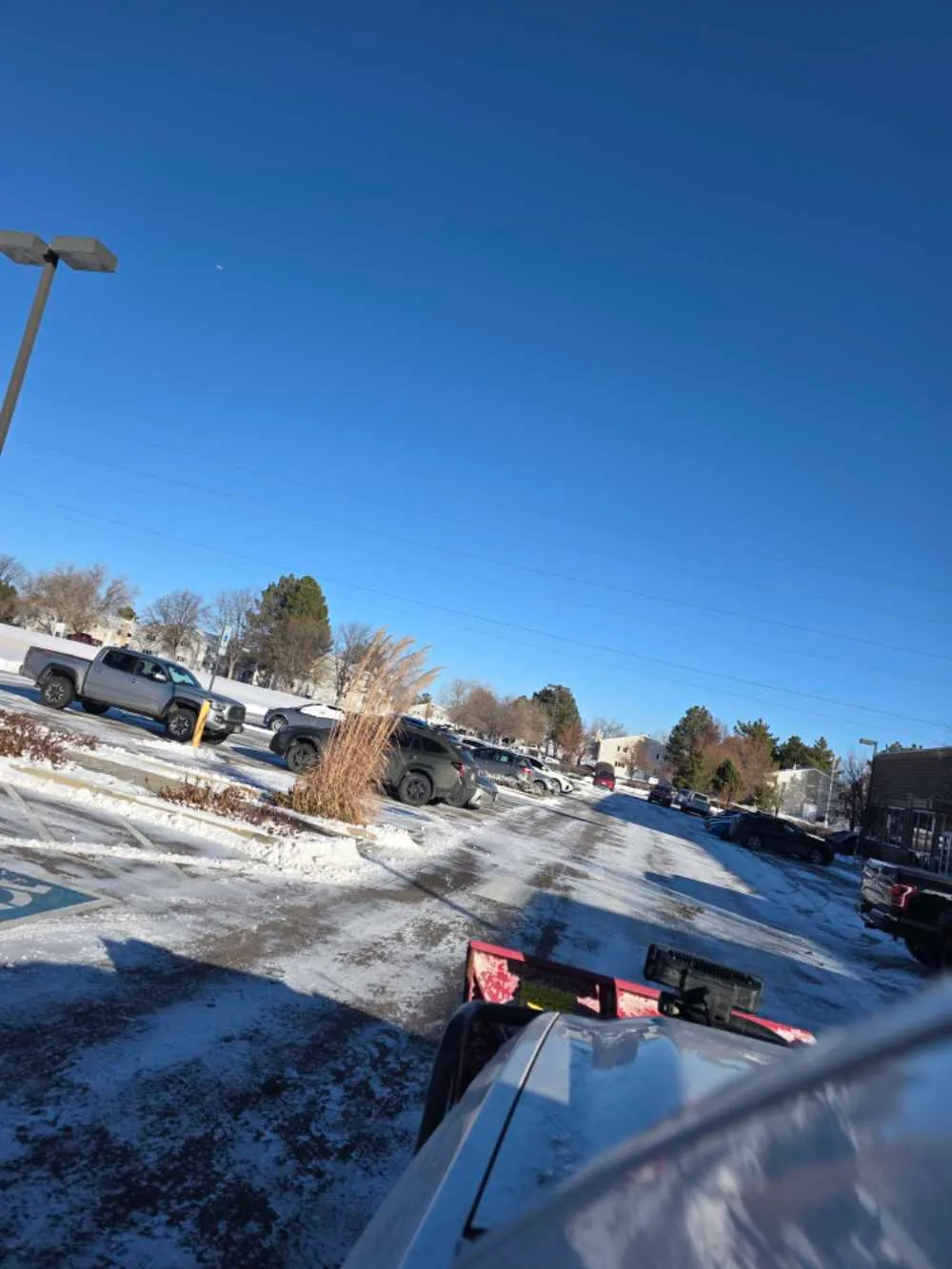 Snow removal truck with plow attachment in a winter parking lot with multiple vehicles and bare trees.