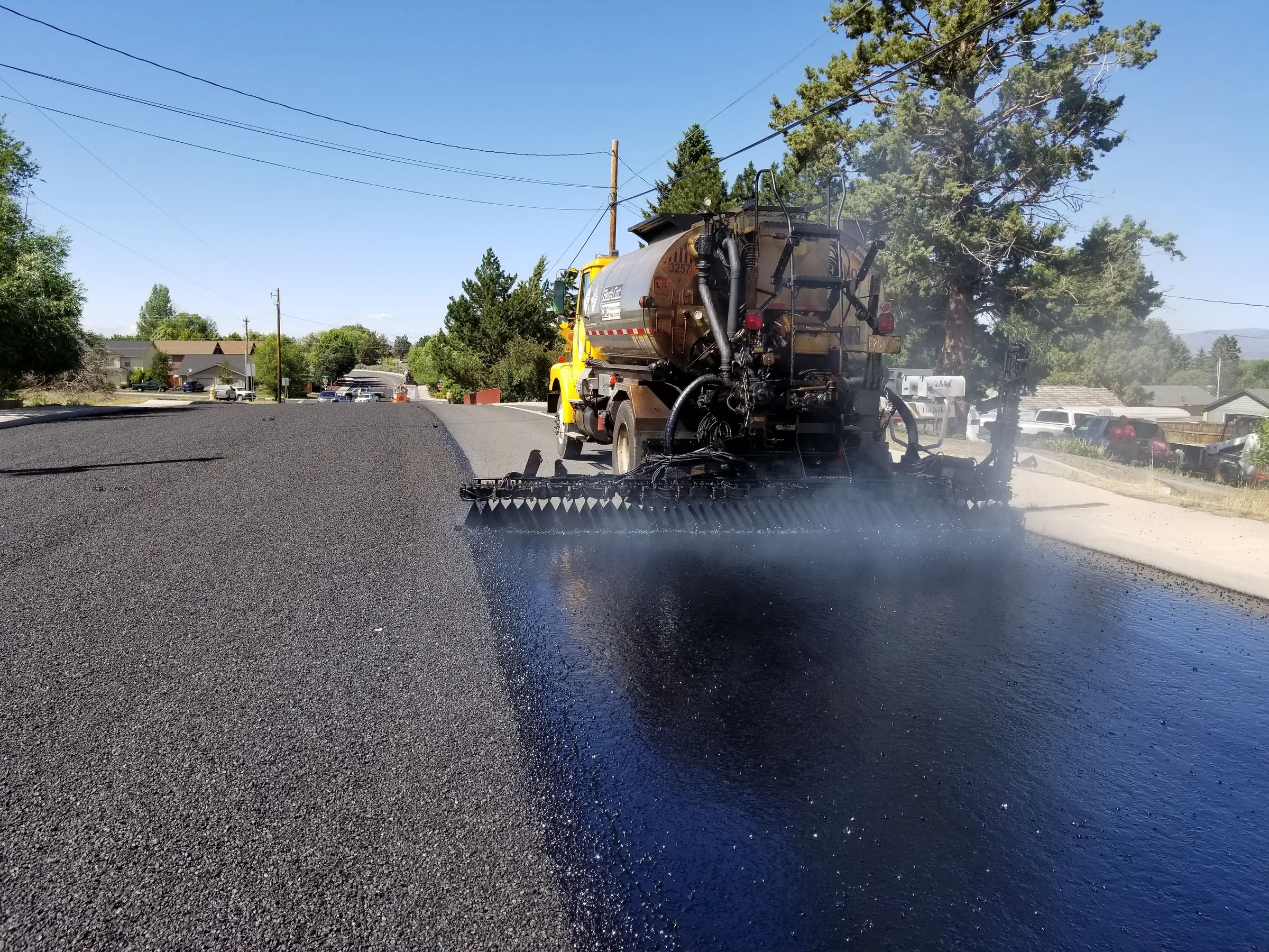 Yellow and brown asphalt paving truck applying fresh blacktop to a residential street.